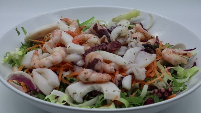 Fresh salad from seafood: octopus, cuttlefish, shrimp. Sea salad on white dish rotating.