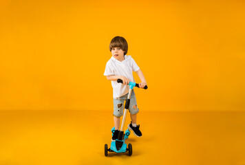 happy little boy riding a scooter on a yellow background with space for text