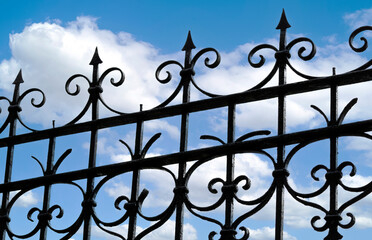 Beautiful decorative cast metal wrought fence against blue sky.