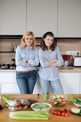 Mom and daughter cooking together in the kitchen. They use vegetables for cooking in a good mood, happy to be together