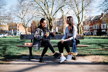 Young girlfriends with coffee chatting on bench