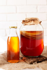 Glass jar with komucha scoby and bottle of ready beverage on light bricked background. Healthy fermented drink. Homemade soft drink.