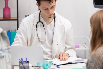 A doctor checks a book calendar for the date of the next follow-up appointment for a young teenage...