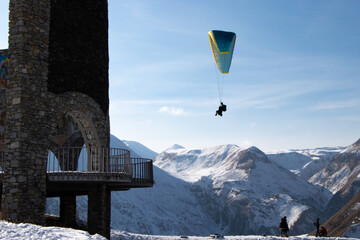 Fototapeta na wymiar Paragliding by Stone Observatory/ Balconies with the Snow-covered Caucasus Mountains of Northern Georgia in the Background - Gudauri, Georgia (Winter)