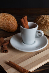 A cup of aromatic black coffee and coffee beans on a wooden table with cinnamon sticks and a French croissant. Coffee break. 