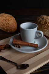 A cup of aromatic black coffee and coffee beans on a wooden table with cinnamon sticks and a French croissant.  A cup of coffee. 