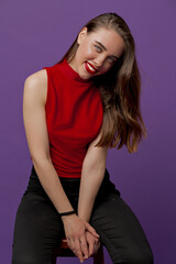 Smiling pretty woman with brown hair wearing red top with red lipstick looking at camera with smile over violet backdrop