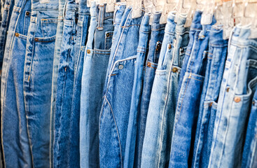 A lot of jeans hang on a hanger in the store. A row of denim pants on a hanger in the store. Sale of jeans in the store on the counter. Jeans texture © Igor Luschay