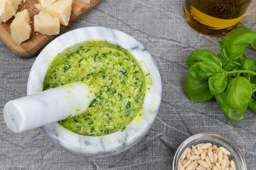 Pesto sauce. Italian pesto prepared in a marble mortar with pestle. Ingredients to prepare the pesto: basil, pine nuts, parmesan, extra virgin olive oil.