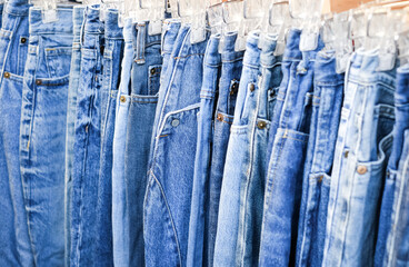 A lot of jeans hang on a hanger in the store. A row of denim pants on a hanger in the store. Sale of jeans in the store on the counter. Jeans texture