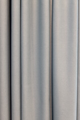Fototapeta premium Gray curtains made of natural silky fabric, with large folds, close-up. Concept details of a modern stylish interior, the use of natural materials in basic universal colors. Vertical