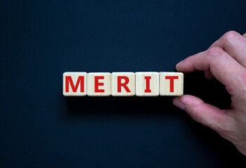 Merit symbol. Wooden cubes with the word 'merit'. Businessman hand. Beautiful black background,...
