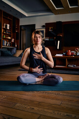 A middle aged woman sitting at home and meditating. Woman doing yoga at home