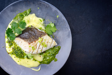 Modern style traditional fried skrei cod fish filet with mashed potato cream and coriander lime relish served as top view on Nordic design plate with copy space right