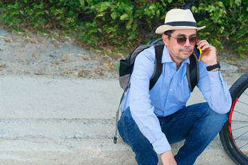 Happy Latino man talking on his cell phone while sitting on the street with his bicycle.