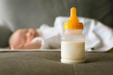 A bottle of milk and a baby sleeping. Formula milk feeding and sleep schedule for infants.