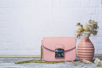 composition of a small handbag in the color of pink powder and a vase on a textured background
