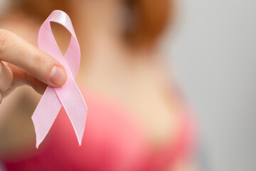 A woman holds a pink ribbon in her hand - Symbol of the fight against breast cancer. - obrazy, fototapety, plakaty