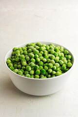Frozen green peas in a white bowl on light background