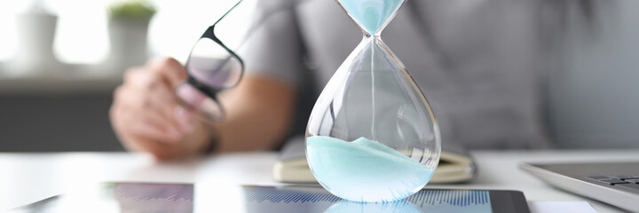 Female hand on desktop holds an hourglass.
