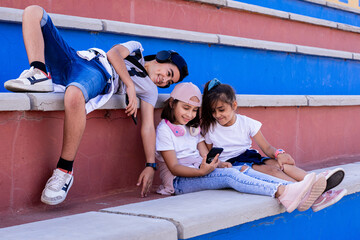 Three small children sitting on the bleachers, with their mobile devices laughing and sharing moments.
