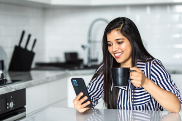 Fototapeta premium Beautiful young woman sitting in the kitchen uses subscription services and media applications.