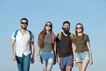 Freinds in jeans and shorts with backpacks walking outdoor. Tourists on nature.