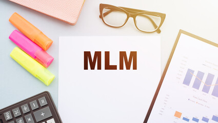 The text MLM - Multi Level Marketing, on office desk with calculator, markers, glasses and financial charts.