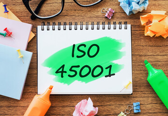 Office wooden table with a notebook ISO 45001 with markers, paper clips, crumpled paper. Business...