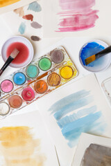 Watercolor paints palette, brushes and papers on table. Creative hobby or art therapy concept.