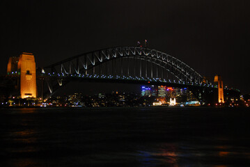 View of the Sydney Harbour Bridge illuminated at night with the city skyline in the background. 