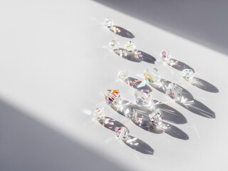 Sparkling glass beads on hard sunlight. Geometrical shadow and rainbow sun beams and reflections on transparent spangles. Jewellery on white background.