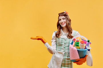 A happy cleaning lady holds a bucket of tools and points her hand at a copy of the space. A bottle of household chemicals and cleaning products. Pin-up style. Yellow background.