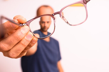 Mature man holds astigmatism glasses with plastic polymer lenses.