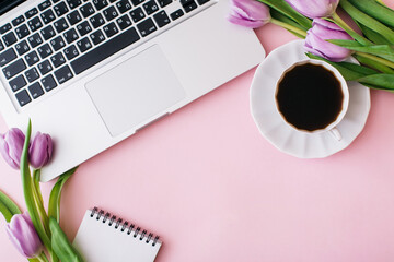 Workspace with laptop, tulip flowers, cup of coffee on pink background. Home office desk. Flat lay, top view, copy space for text. Spring concept.