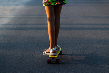 Defocus skater girl moving along asphalt road on a yellow skateboard wearing white sandals and...