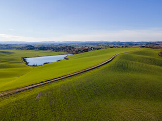 Aerial view of a calm landscape with green hills, dirt road and a lake. Drone shot  