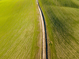 Aerial view of a dirt road in the middle of a green field. Drone shot. 