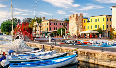 Bardolino, Italy, 10/28/2019: Boats in old town port of Bardolino and tourists walking and sitting...