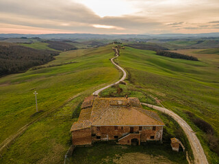 An abandoned house at the end of a dirt road at sunset light. Drone view, aerial shot.
