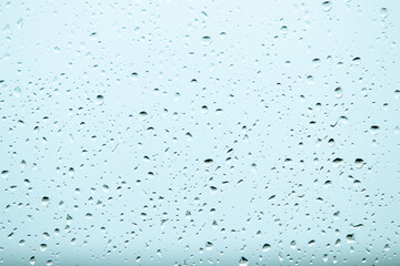 Rain water drops on window glass with blue toned background.