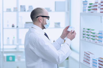 Man pharmacist in protective face mask working in drugstore