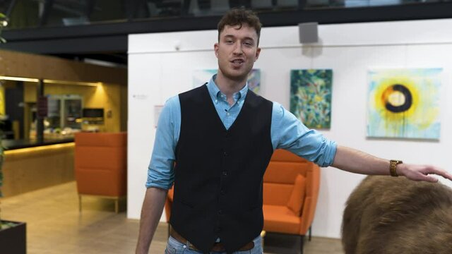 Young businessman in a waistcoat petting a llama in an office,scared.