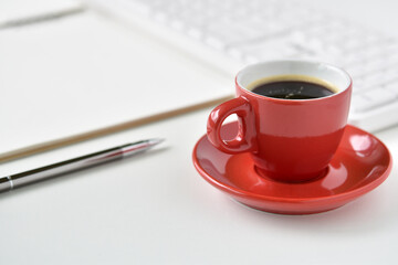 Black coffee in red cup on table desk with silver pencil, sketchbook and keyboard is elements.