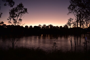 Wide slow-flowing river at dusk with tree silhouettes