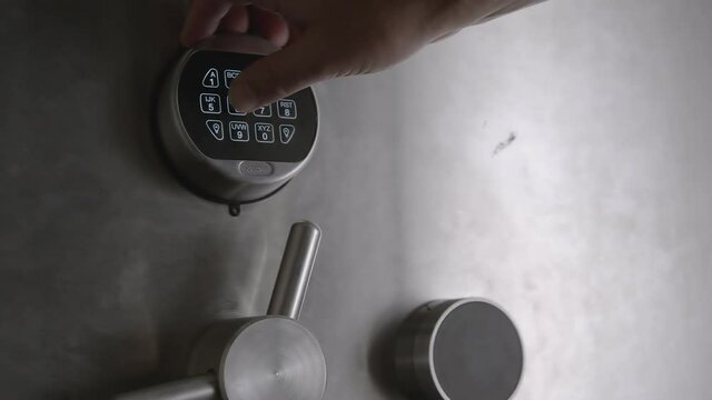 A man's hand punches in a combination on a keypad and then proceeds to open a safe door.