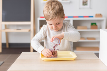Little boy at Montessori school pouring beans from one container to another; practical life skills work 