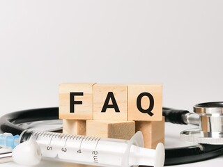 Phrase FAQ written on wooden cubes with stethoscope and syringe. Medical and health concept.