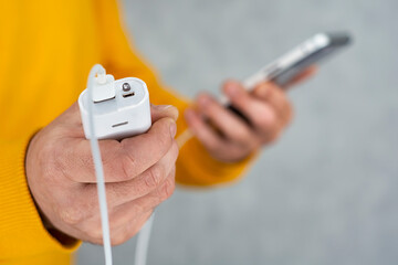 Man holds a smartphone and a portable charger in his hands on a gray background. Power Bank charges the phone.