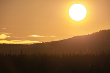 The bright, yellow, orange sun setting over the dark silhouette of mountains in northern Canada...